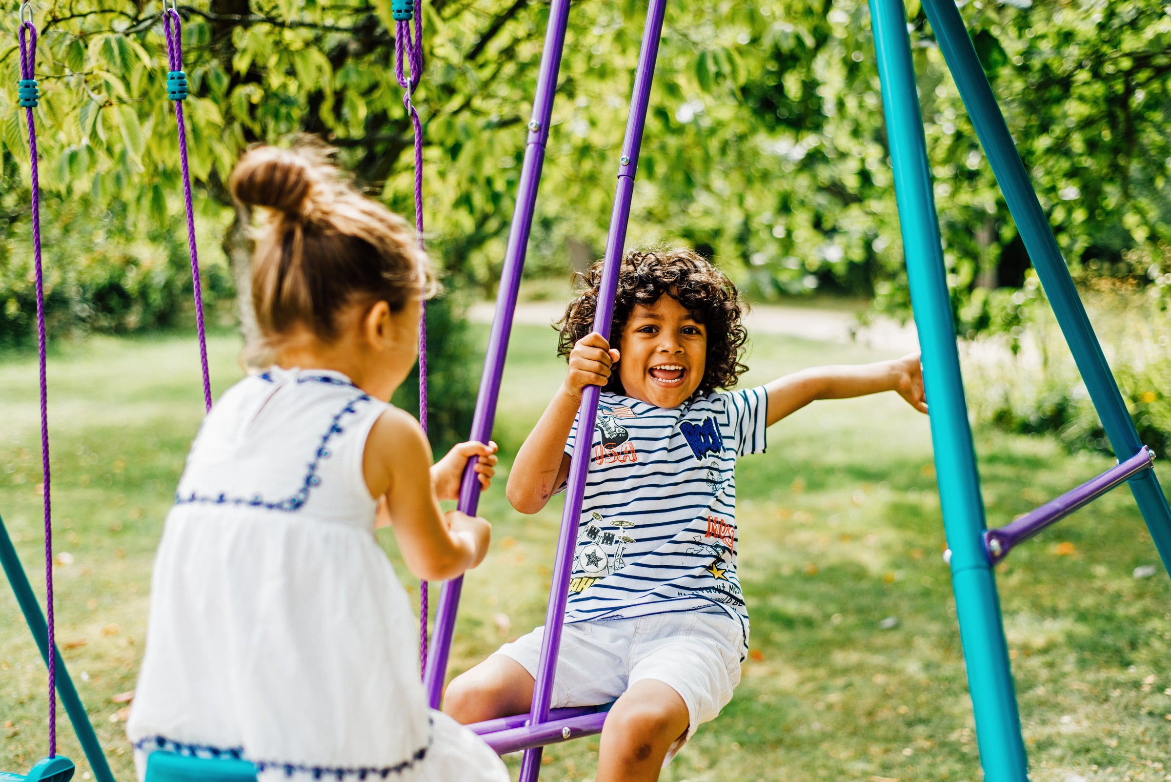 Plum wooden and metal swing sets in garden for kids outdoor play including single and double swings