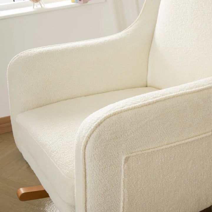 Close-up of a off white nursing chair with wooden legs in a room.