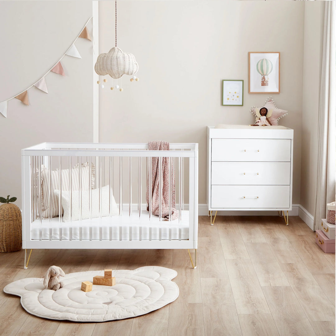 Nursery room with white crib and dresser in a well-lit room.