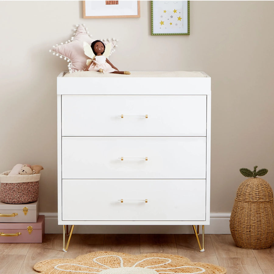 White dresser with gold legs in a nursery setting with toys and decor.