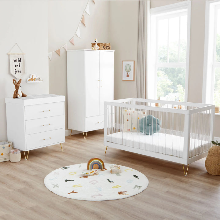 Nursery room with white crib, dresser, and wardrobe in a bright room.