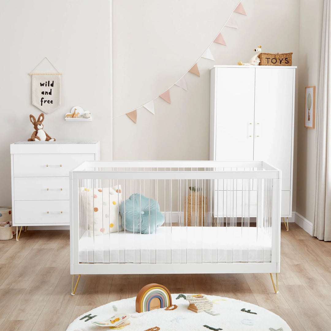 Nursery room with white crib, dresser, and toys on a wooden floor.