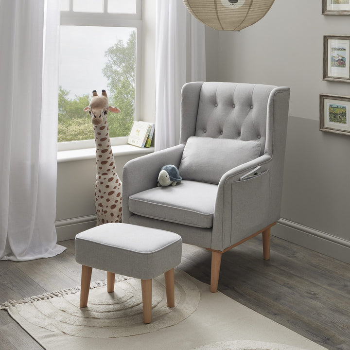 Grey armchair with ottoman in a room with large windows and decorative elements.