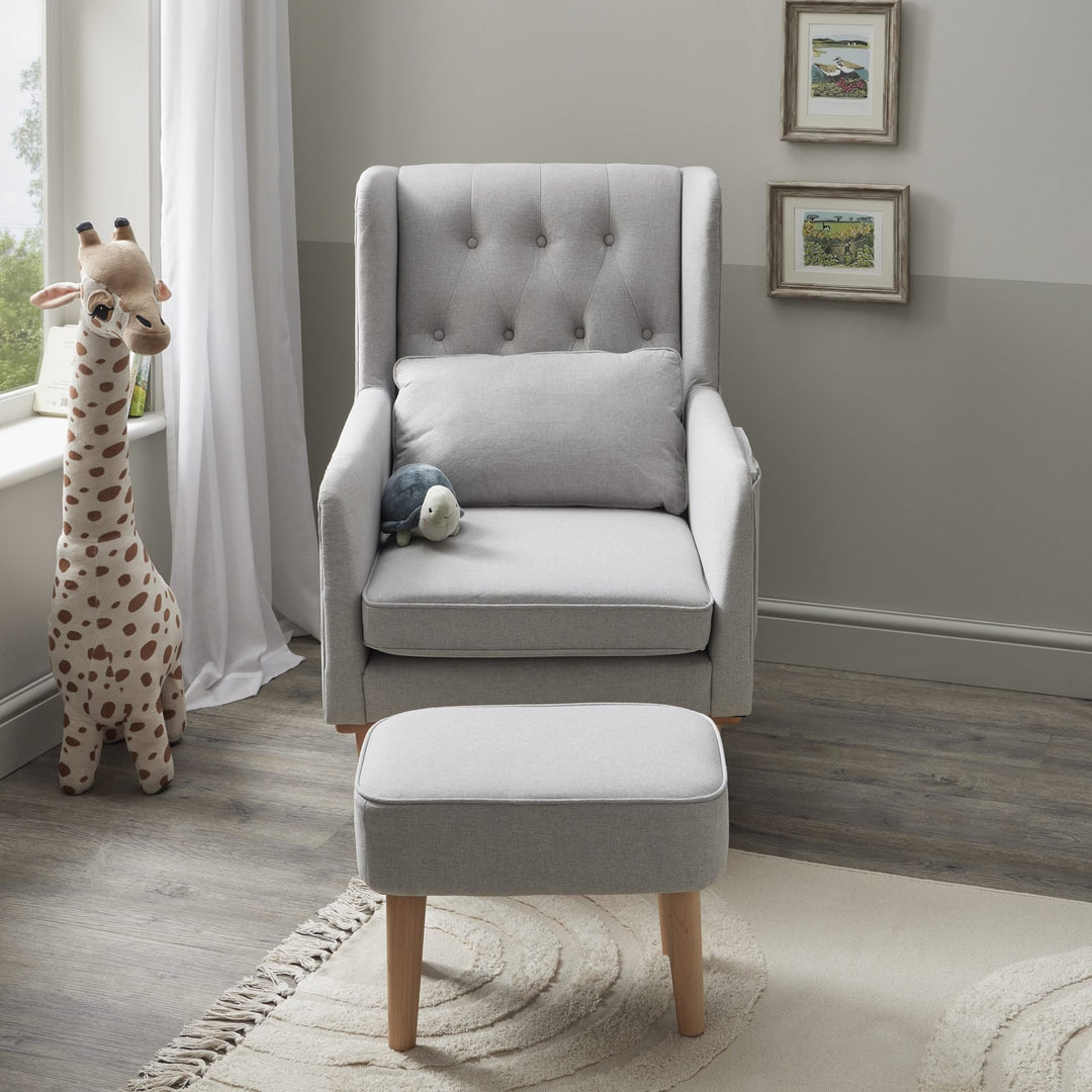 Grey upholstered chair with ottoman in a room with a window and framed pictures on the wall.