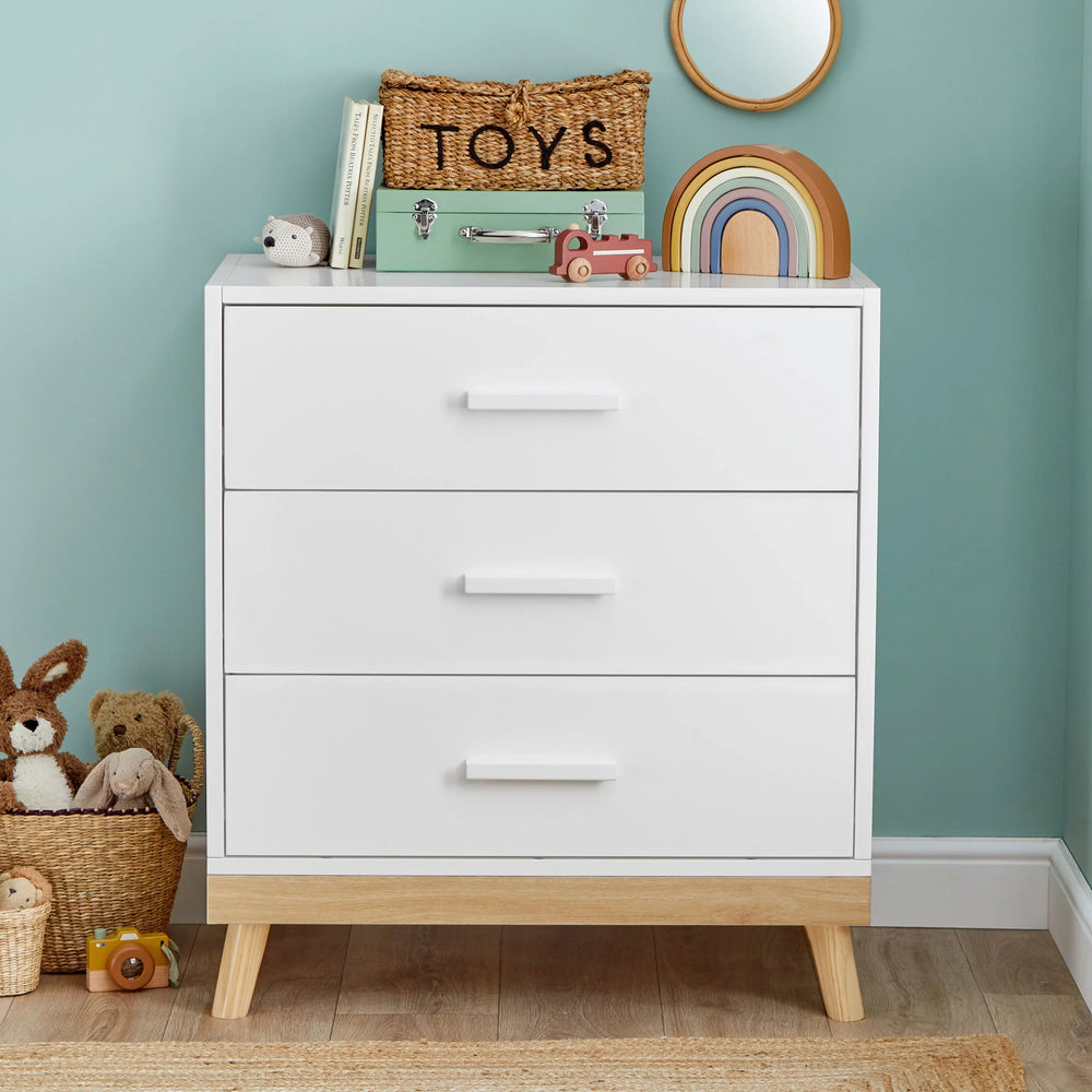 White dresser with wooden legs in a room with toys and a 'TOYS' sign on a green wall.