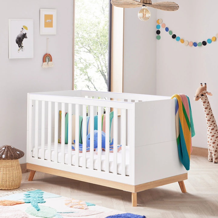 White crib in a nursery with colourful bedding and decor