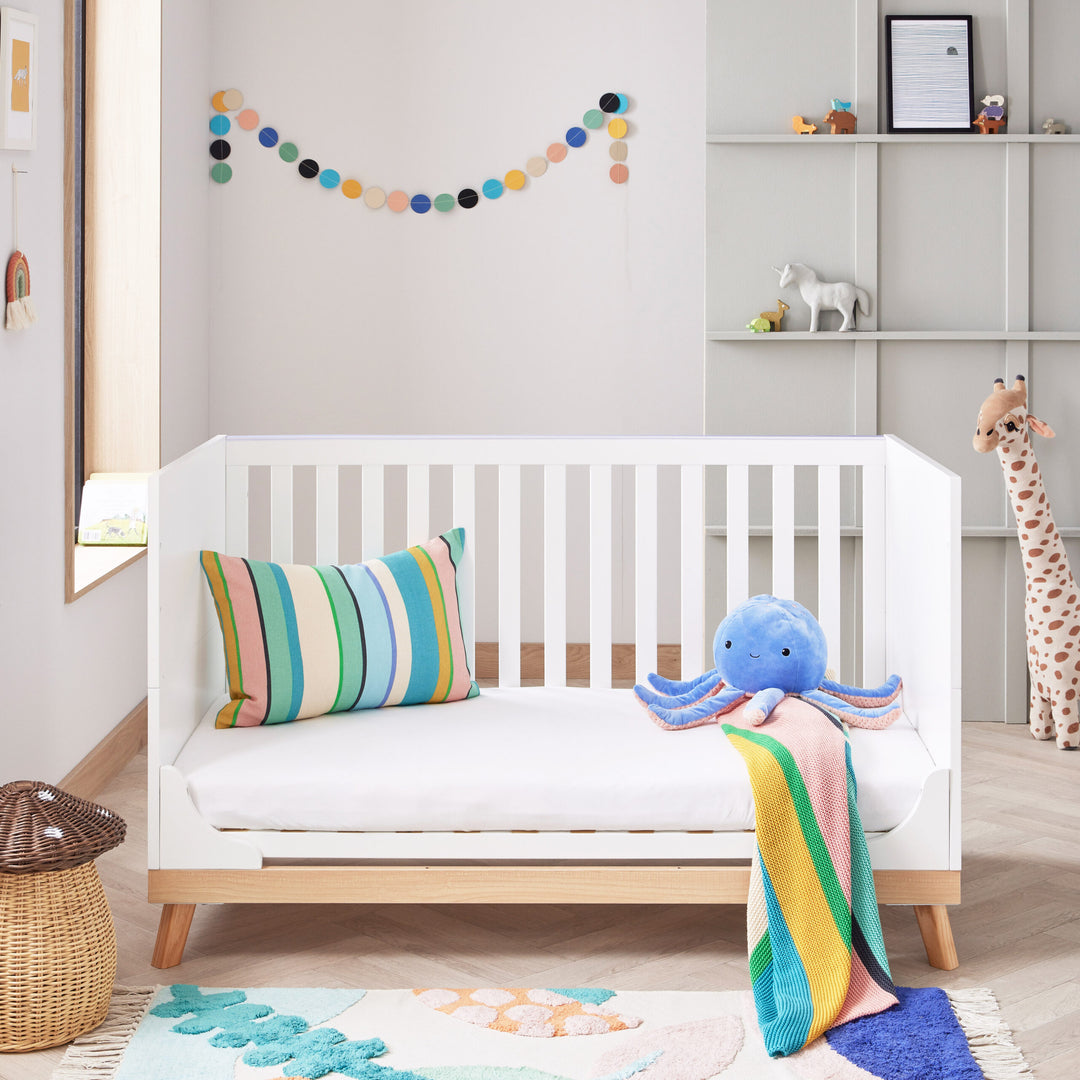 Children's room with a white crib, colourful pillow, and plush octopus toy.