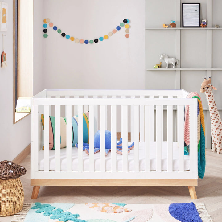 White crib in a child's room with colourful decor and toys.