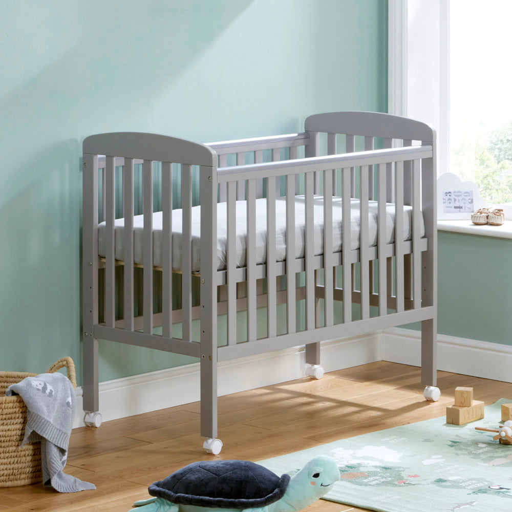 Grey crib in a room with a light green wall and wooden floor.