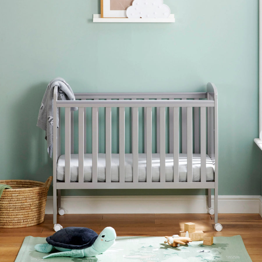 Gray crib in a room with a light green wall and wooden floor.