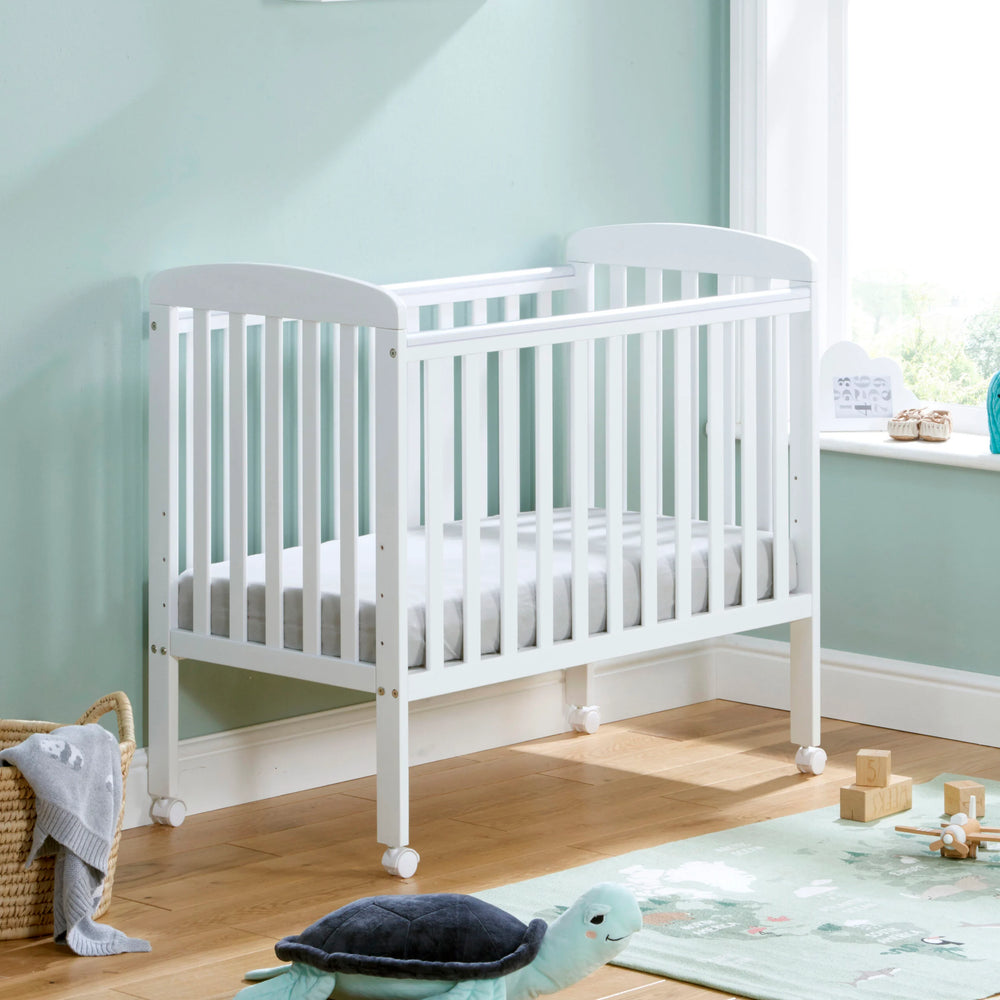 White crib in a nursery with light blue walls and wooden floor.
