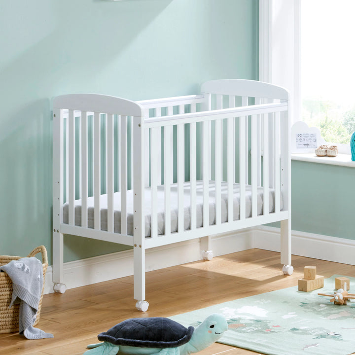 White crib in a nursery with light blue walls and wooden floor.