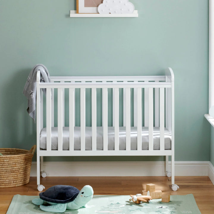 White crib in a room with a green wall and wooden floor.