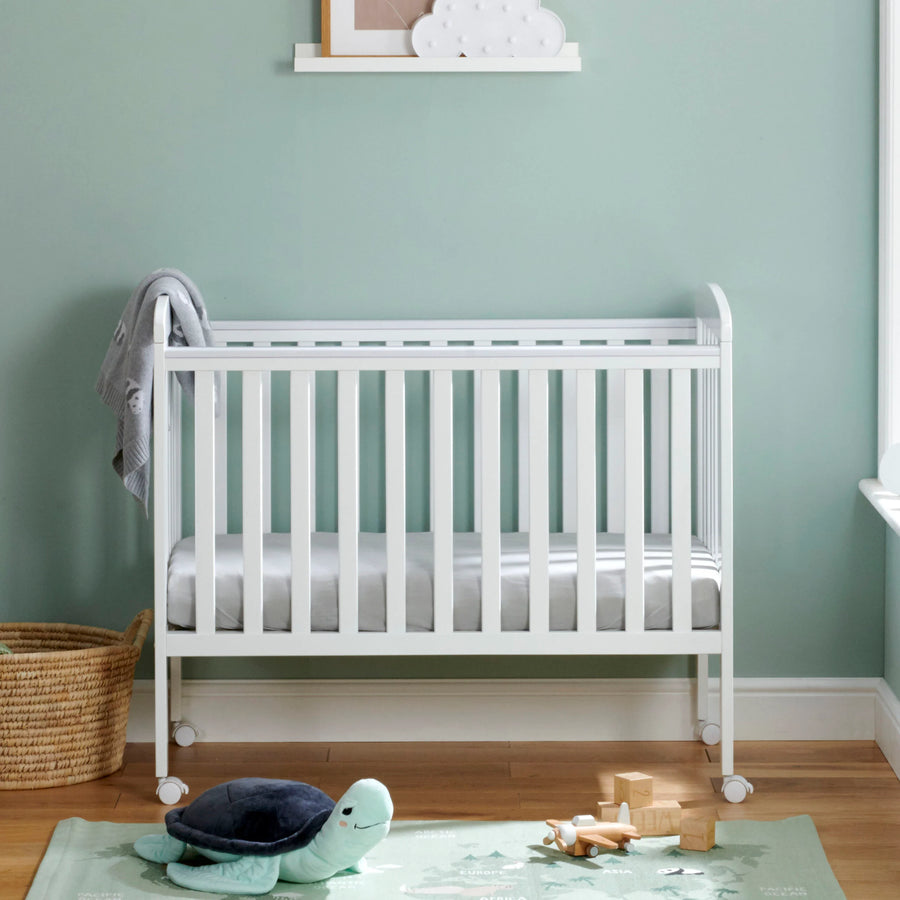 White crib in a room with a green wall and wooden floor.