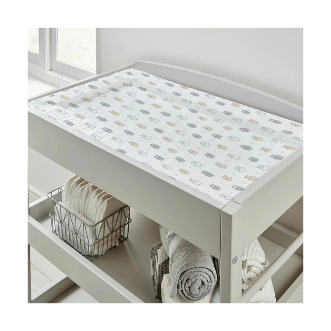 Nursery changing table with a patterned cover and folded towels underneath.