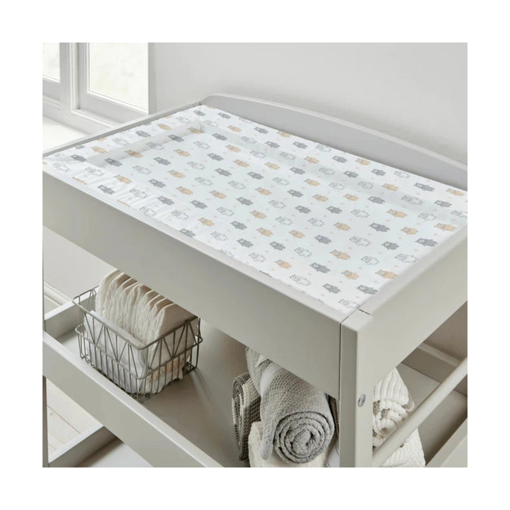 Nursery changing table with a patterned cover and folded towels underneath.