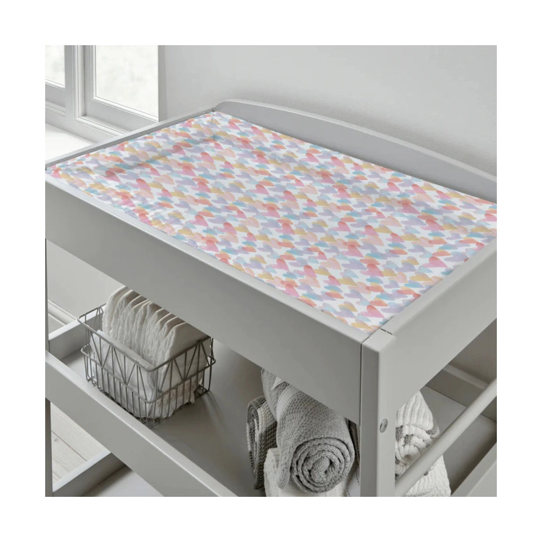 Grey changing table with a colourful geometric patterned cover, towels, and a basket in a bathroom setting.