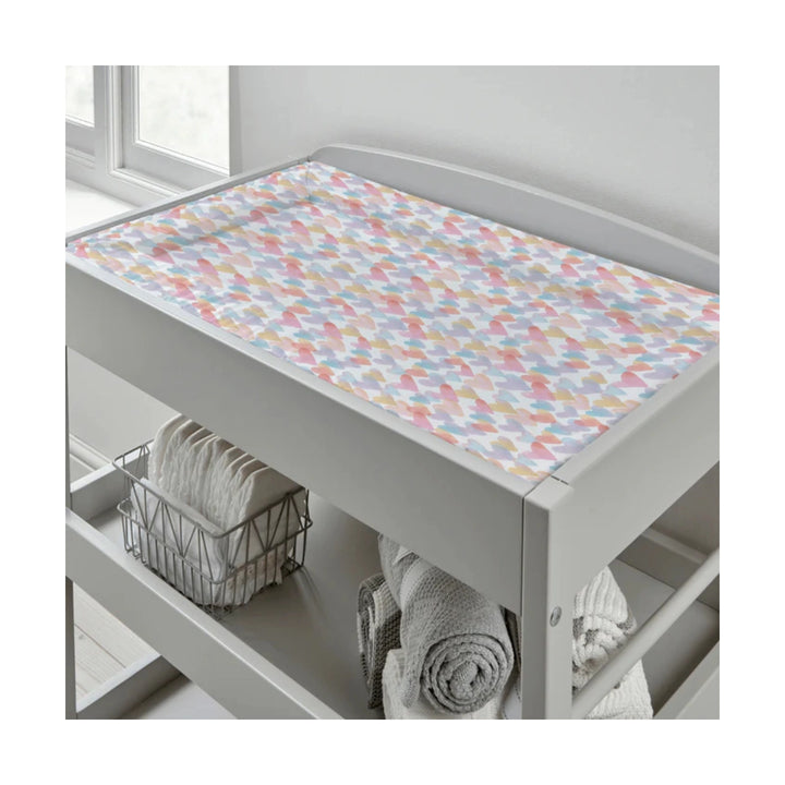 Grey changing table with a colourful geometric patterned cover, towels, and a basket in a bathroom setting.