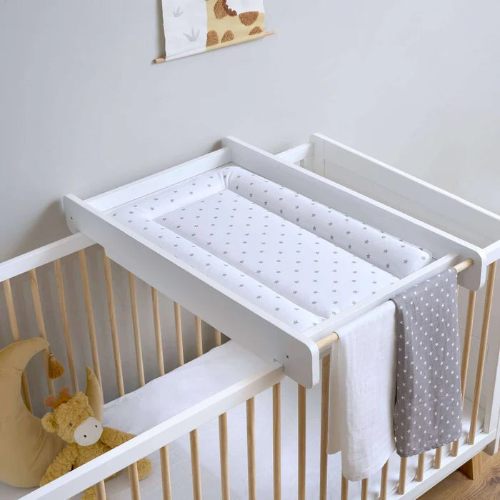 White crib with changing table attached against a light gray wall.
