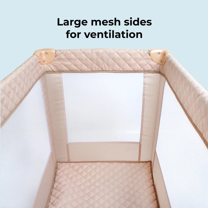 My Babiie Travel Cot in Blush Quilted with large mesh sides for ventilation on a light blue background