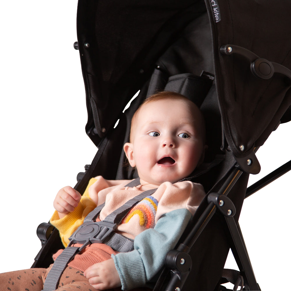 Baby sitting in Red Kite Push Me 2U midnight stroller  with a white background