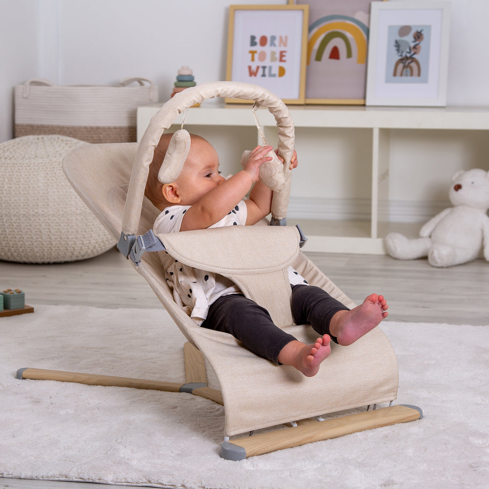 Baby in a Red Kite Baya Bouncer in a room with toys and decorations.