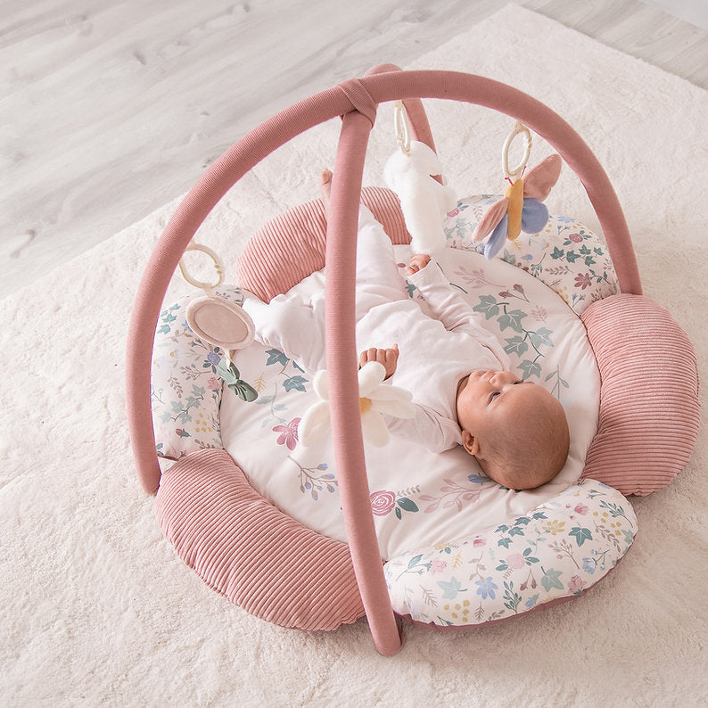 Baby in a Red Kite Play Gym Rose & Ivy on a light wooden floor.
