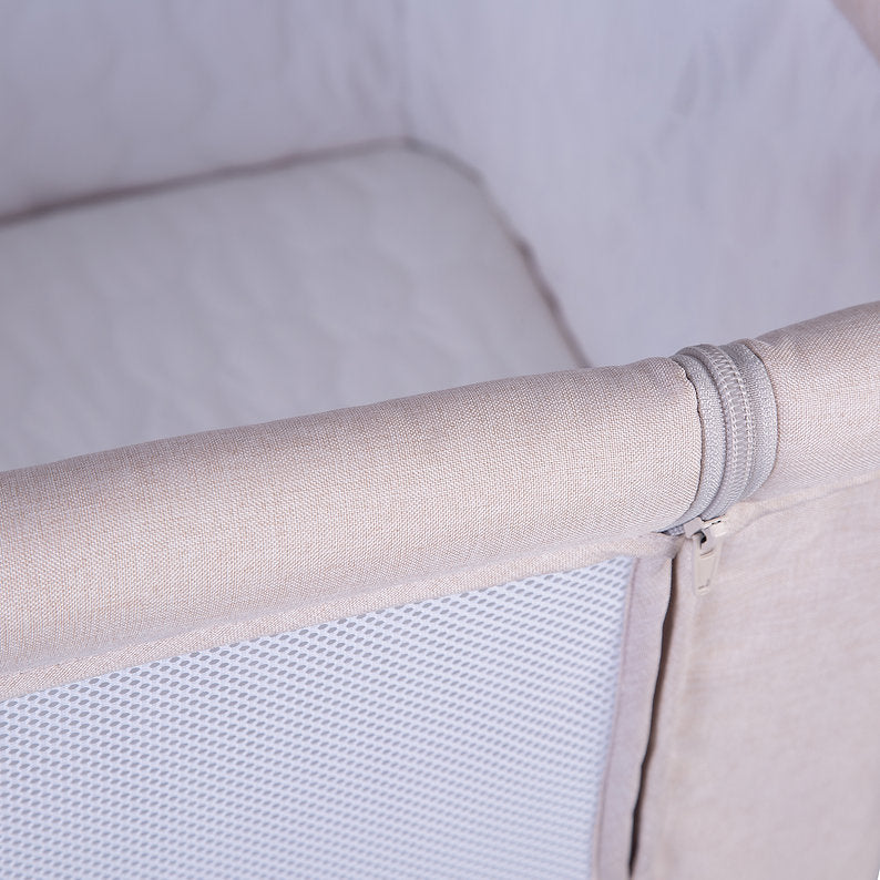 Red Kite Rockabye Bedside Crib Close-up of a baby crib bumper with beige fabric and mesh panel.