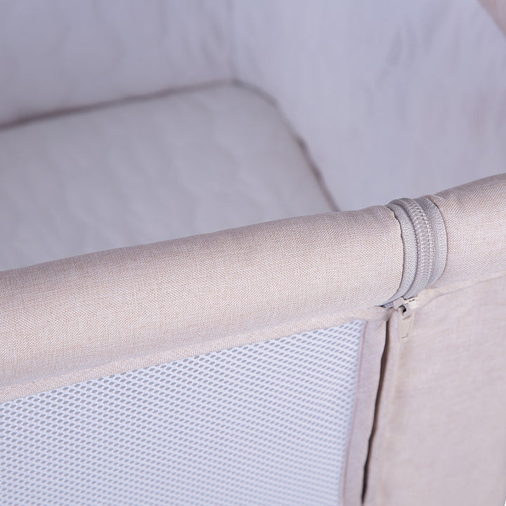 Red Kite Rockabye Bedside Crib Close-up of a baby crib bumper with beige fabric and mesh panel.