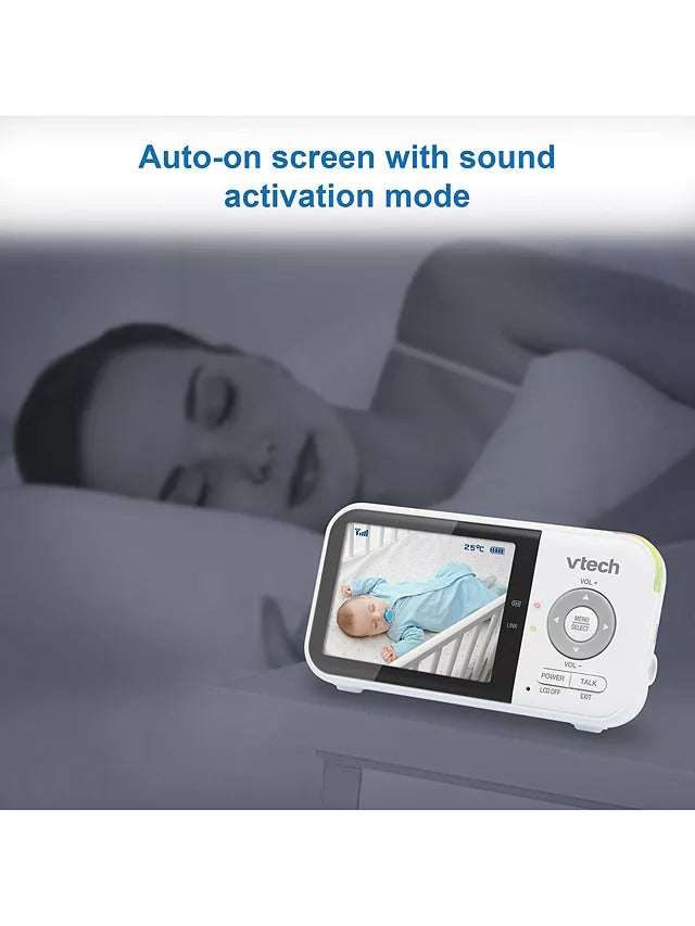Baby monitor with screen displaying a baby and room temperature, placed on a surface with a child lying nearby.