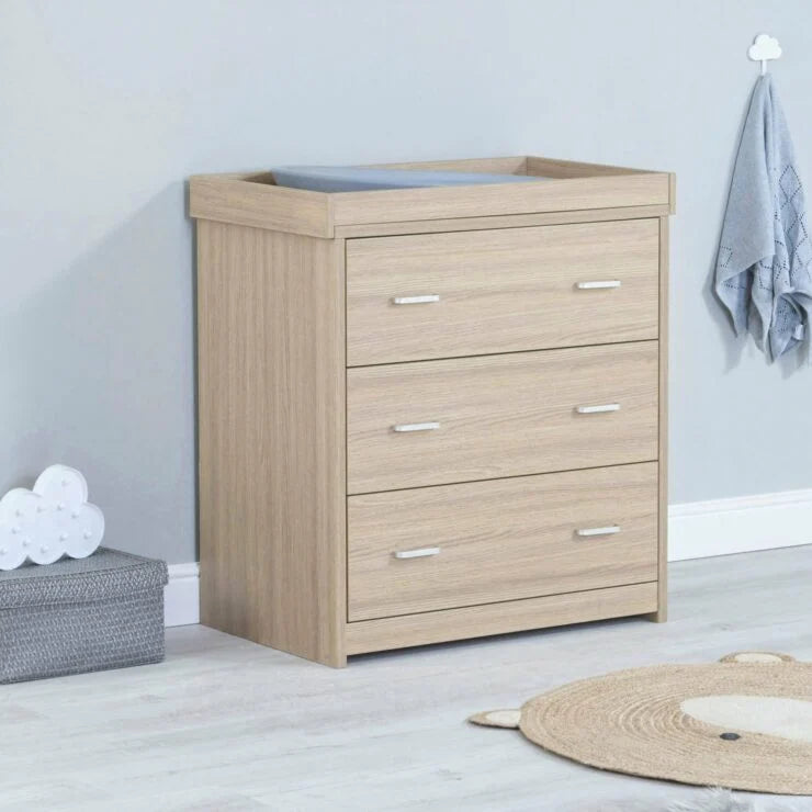 Wooden dresser with three drawers in a room setting with a rug and storage box.