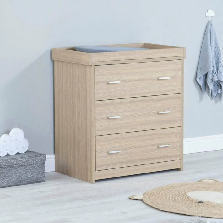 Wooden dresser with three drawers in a room setting with a rug and storage box.