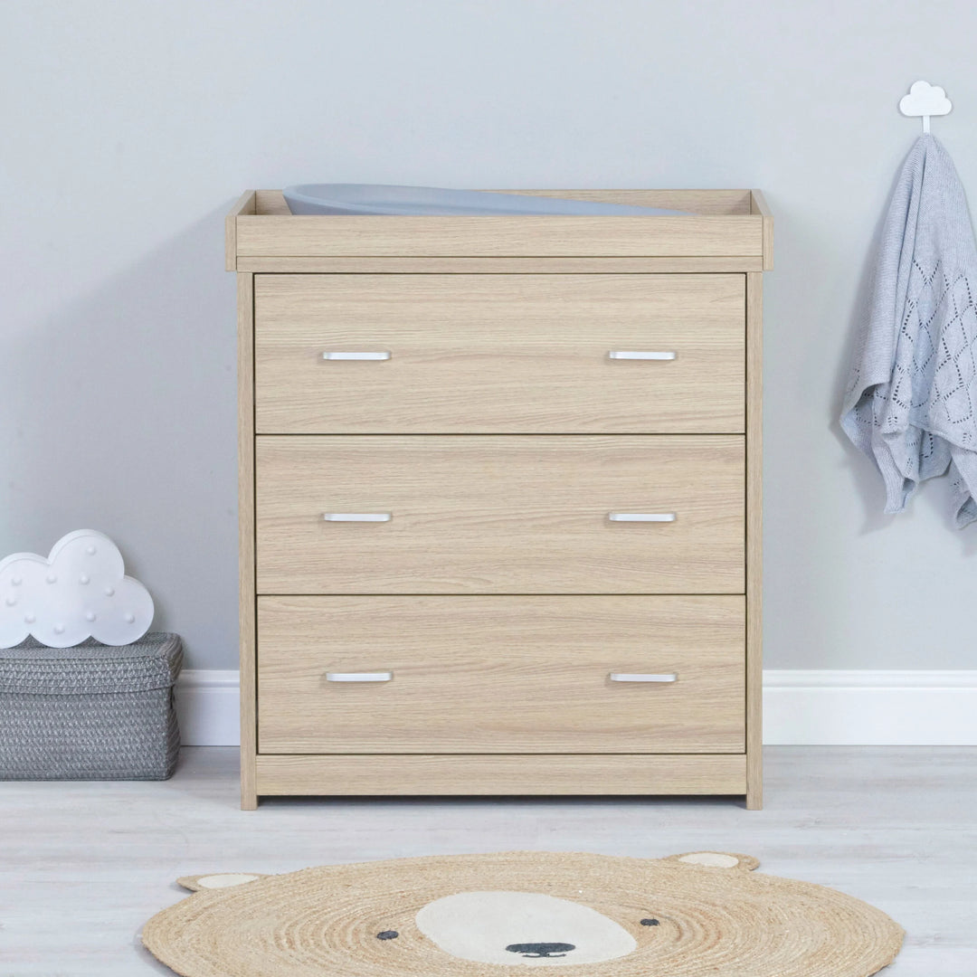 Wooden changing table in a nursery with a light gray wall and decorative items.