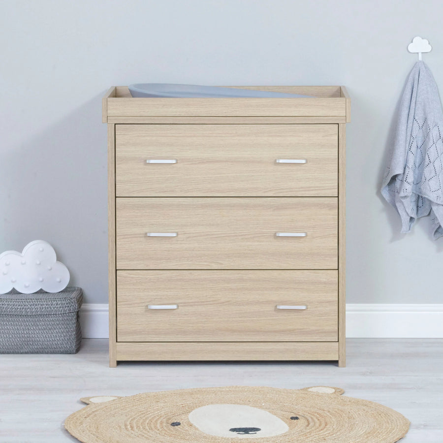Wooden changing table in a nursery with a light gray wall and decorative items.